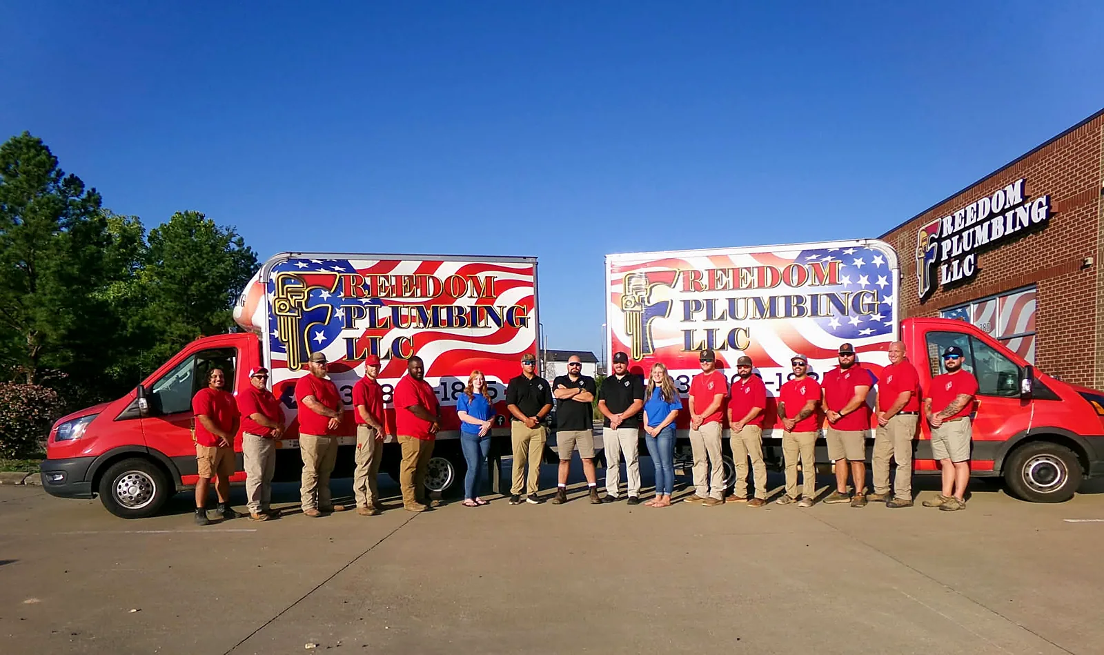 The Freedom Plumbing crew lined up in front of two company trucks at the shop