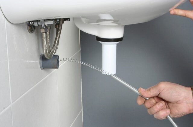A plumber feeding a drain snake into a kitchen sink to clear a clog
